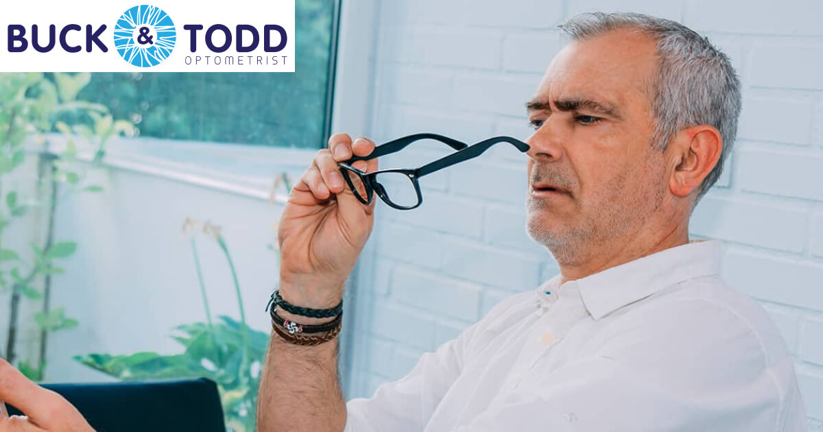 A man peers through his glasses, comparing his vision with and without them while holding a smartphone