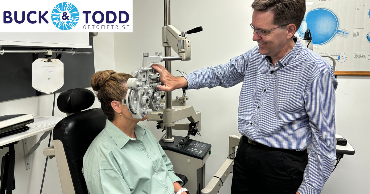 An optometrist examines a patient using a slit lamp biomicroscope in a clinic with educational eye diagrams in the background